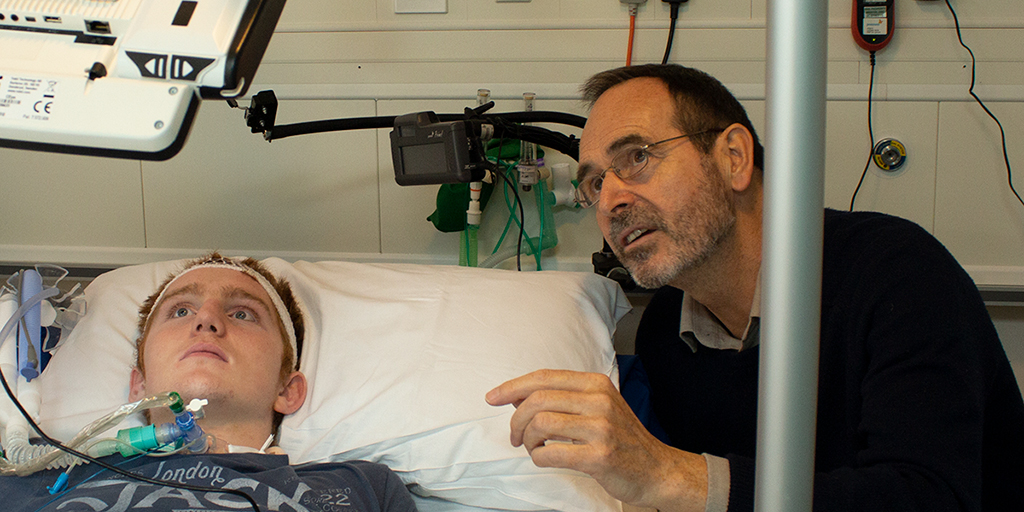man talking to patient in hospital bed, both looking at overhead screen