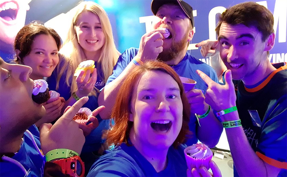 Six smiling figures in charity shirts eating cupcakes