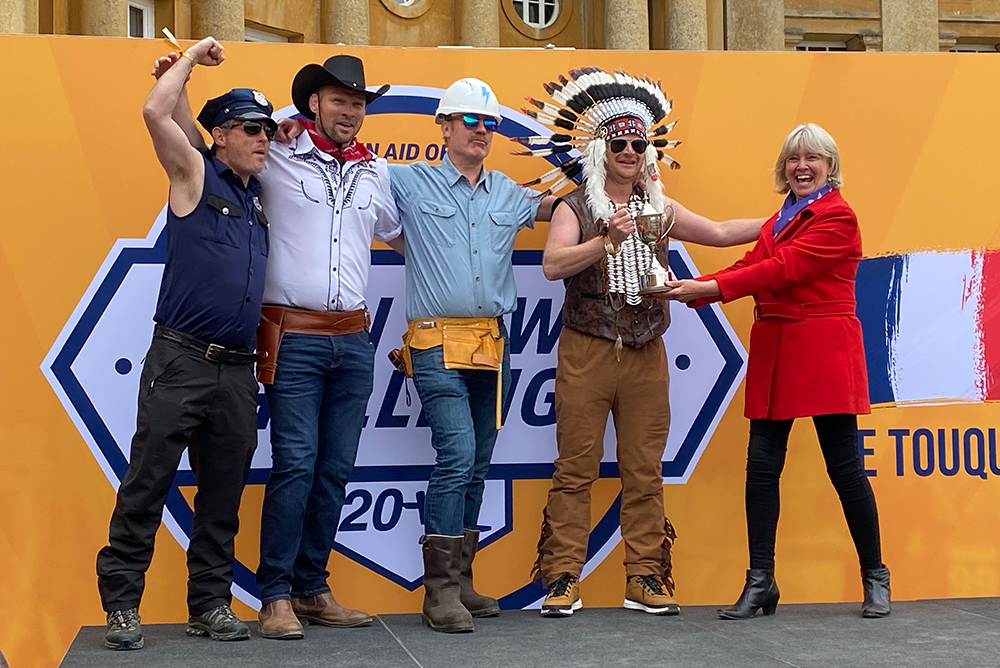 Woman presents trophy to four men dressed as the pop group The Village People