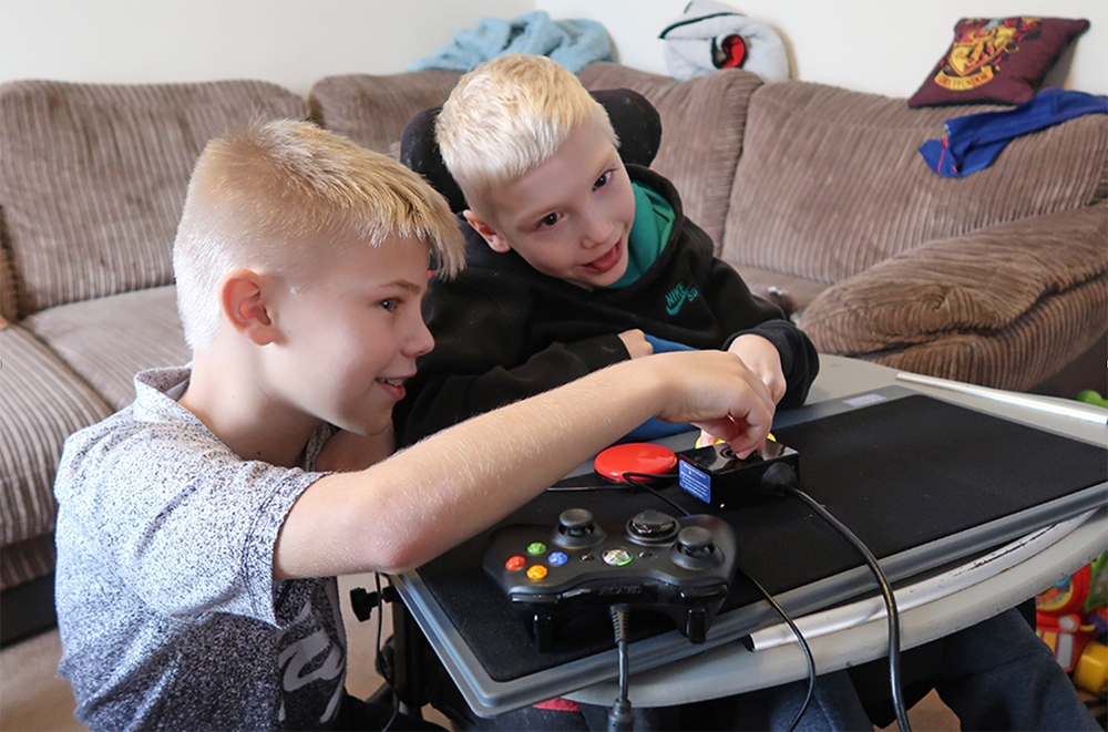 One young boy helping another to play video games with adapted setup