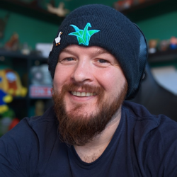 A man wearing a blue beanie with a crane bird on it smiles at the camera