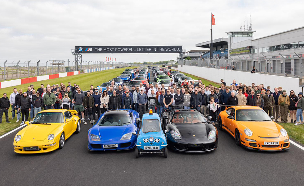 Over 40 high performance cars lined up on a race track with large group of people