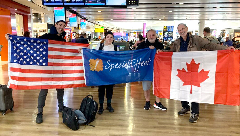 Four people in an airport holding SpecialEffect, US and Canadian flags