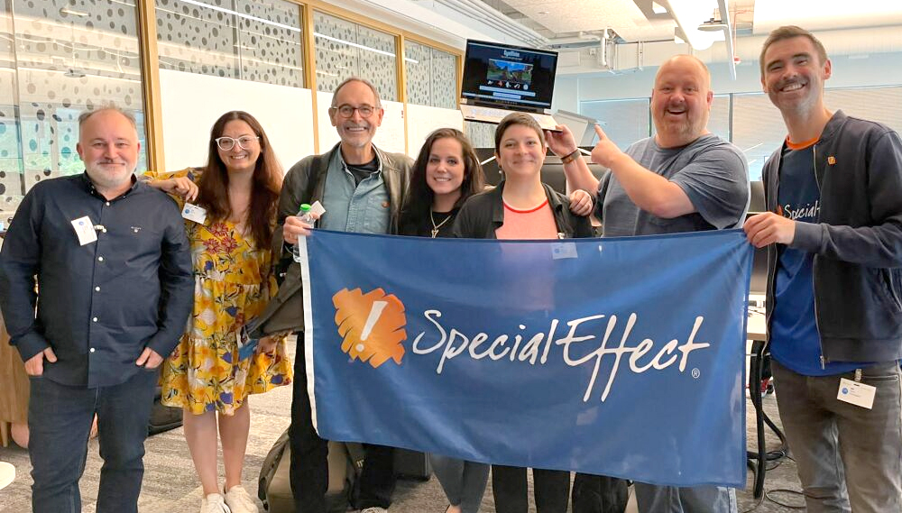 Seven smiling people holding a SpecialEffect flag 