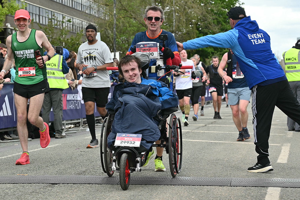 Runner pushes man in sports wheelchair over the finishing line