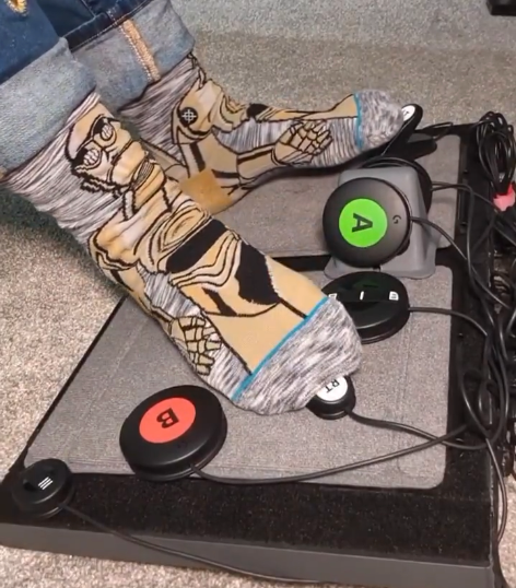 Close up of sock-clad feet pressing down on two of ten buttons positioned of a footboard 