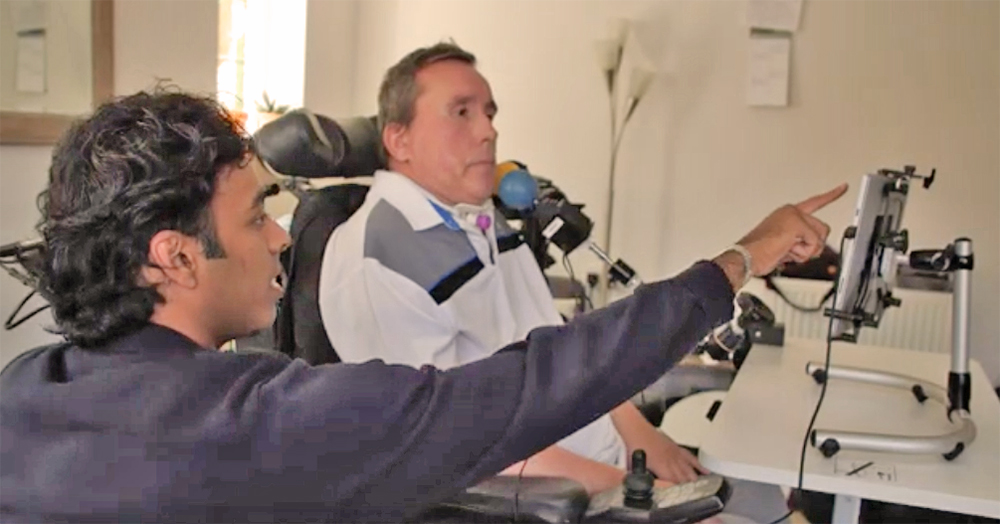 Therapist pointing at screen as man using assistive technology watches