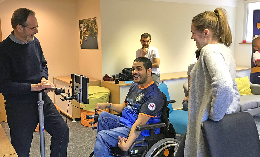 Man in a wheelchair looks at computer, surrounded by three adults