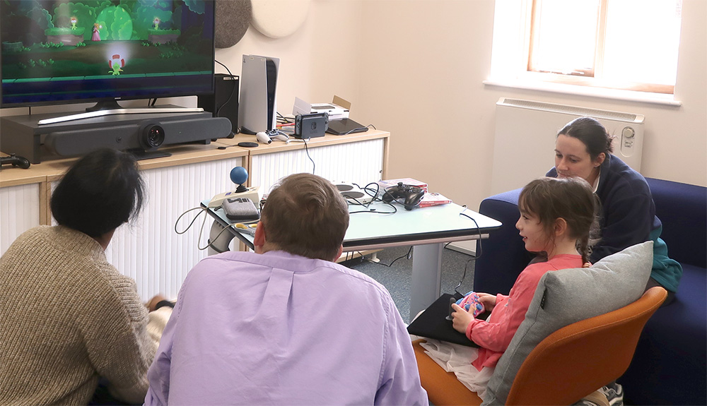 Three adults and a young girl look at a screen showing Princess Peach game