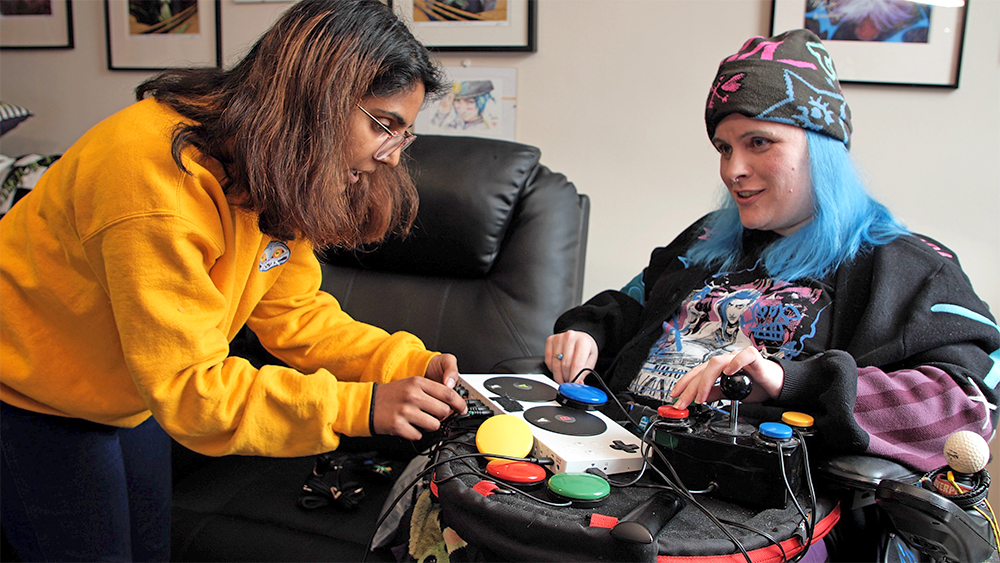 Therapist adjusts technology on the wheelchair lap tray of a woman wearing a beanie